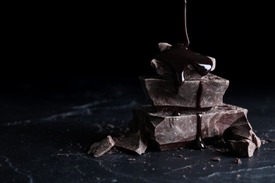 Pouring syrup onto pieces of dark chocolate on black table, closeup