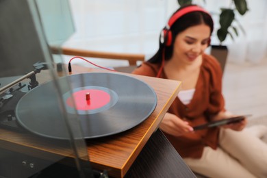 Woman listening to music at home, focus on turntable