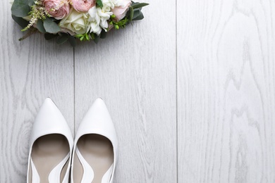 Pair of wedding high heel shoes and beautiful bouquet on white wooden floor, flat lay. Space for text
