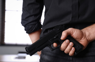 Photo of Man holding gun indoors, closeup. Dangerous criminal