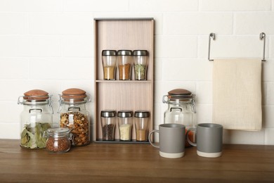 Photo of Set of spices and different dishware on wooden table near white brick wall in kitchen