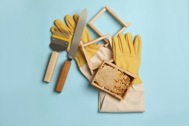 Hive frame with honeycomb and beekeeping equipment on light blue background, flat lay