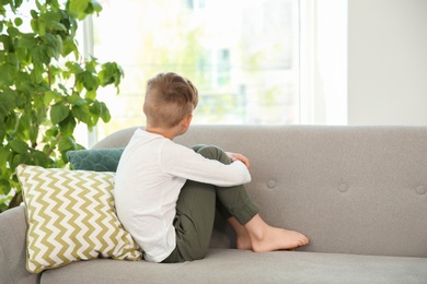 Lonely little boy sitting on couch at home. Autism concept