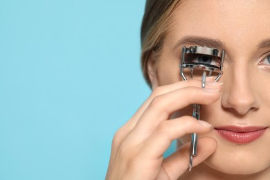 Young woman using eyelash curler on light blue background, closeup. Space for text