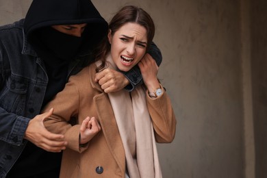 Woman defending herself from attacker near beige wall outdoors