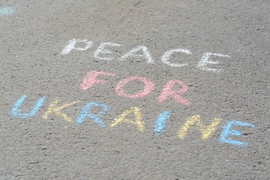 Photo of Words Peace For Ukraine written with colorful chalks on asphalt outdoors