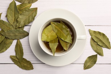 Photo of Cup of freshly brewed tea with bay leaves on white wooden table, flat lay