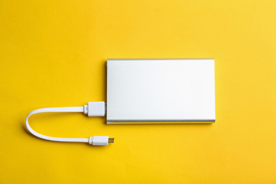 Modern portable charger with cable on yellow background, top view