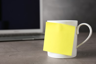 Cup with blank sticky note on grey table. Space for text