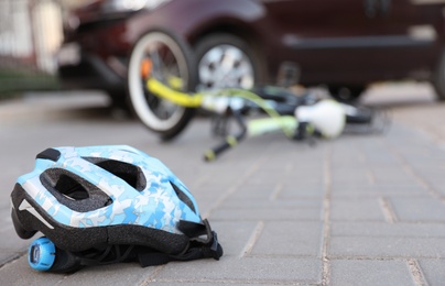 Fallen bicycle after car accident outdoors, focus on helmet