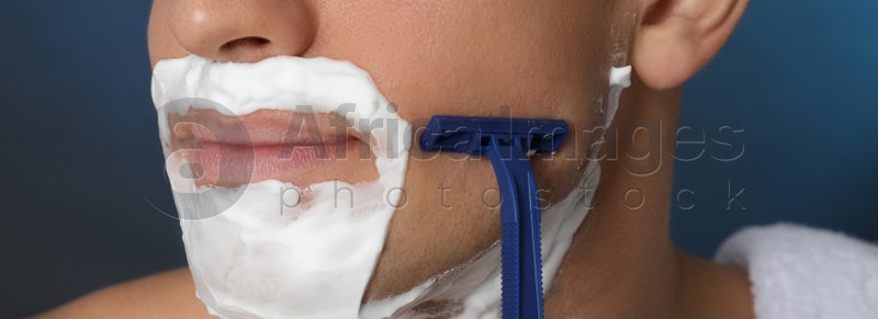 Man shaving with razor on blue background, closeup. Banner design