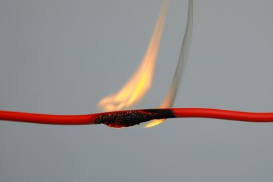 Inflamed red wire on grey background, closeup. Electrical short circuit