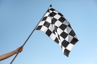 Woman holding checkered finish flag on light blue background, closeup