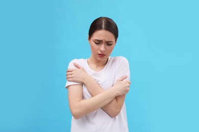 Woman suffering from fever on light blue background. Cold symptoms