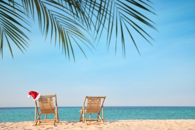 Photo of Sun loungers and Santa's hat on beach, space for text. Christmas vacation