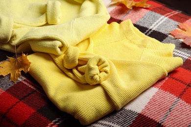 Photo of Beautiful yellow warm sweater and leaves on checkered plaid, closeup