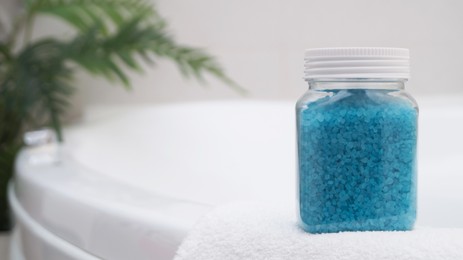 Jar with sea salt and fluffy towel on bath. Space for text