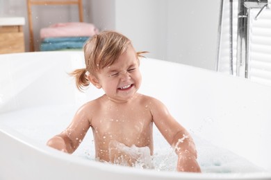 Photo of Cute little girl playing in bathtub at home