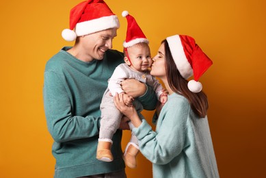 Happy couple with cute baby wearing Santa hats on yellow background. Christmas season