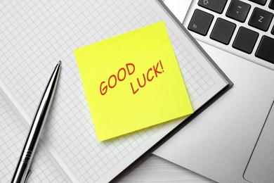 Sticky note with phrase GOOD LUCK, notebook, pen and laptop on white wooden table, top view