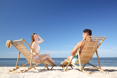 Woman in bikini and her boyfriend on deck chairs at beach. Happy couple