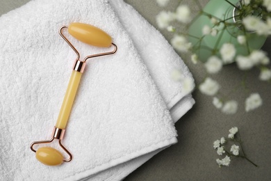 Natural jade face roller, towel and flowers on grey background, flat lay