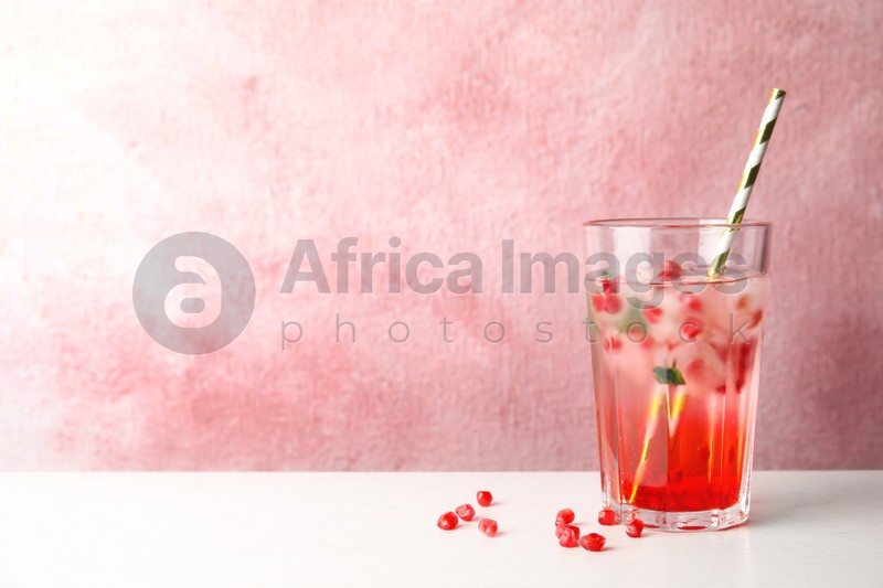Tasty cocktail with pomegranate ice cubes on table against color background. Space for text