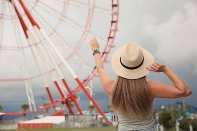Photo of Woman near beautiful large Ferris wheel outdoors, back view. Space for text
