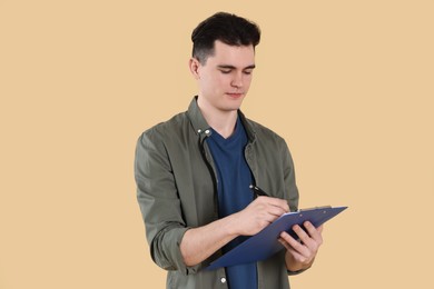 Handsome young man writing on clipboard against beige background