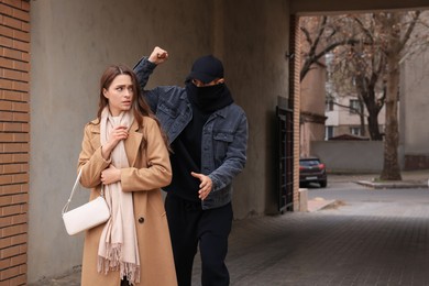 Criminal attacking young woman in alley, space for text. Self defense concept