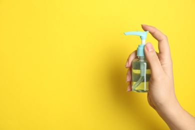 Photo of Woman holding antiseptic gel on yellow background, closeup. Space for text
