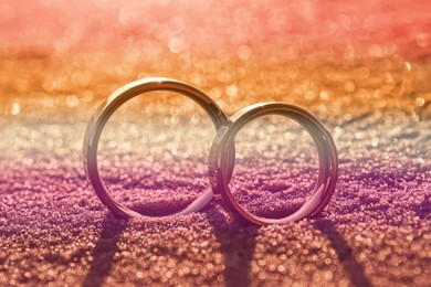 Double exposure of lesbian flag and wedding rings on sandy beach, closeup