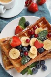 Photo of Delicious Belgian waffles with berries and banana on plate, top view