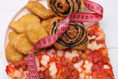 Photo of Different unhealthy food and measuring tape on white wooden table, top view. Weight loss concept