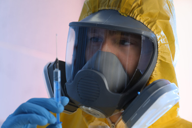Scientist in chemical protective suit with syringe on color background, closeup