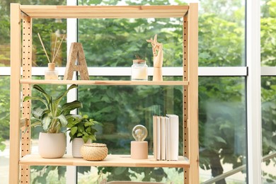 Wooden shelving unit with beautiful houseplants, books and air reed freshener indoors