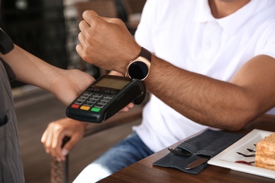 Photo of Man making payment with smart watch in cafe, closeup