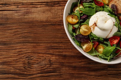Delicious burrata salad with colorful cherry tomatoes, croutons and arugula on wooden table, top view. Space for text