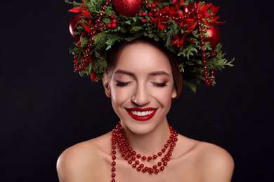 Beautiful young woman wearing Christmas wreath on black background