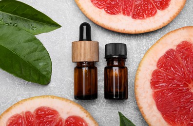 Bottles of essential oil with grapefruit slices and leaves on grey table, flat lay