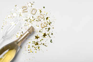 Bottle of sparkling wine, glass, golden confetti and number 2023 on white background, flat lay with space for text. Happy New Year