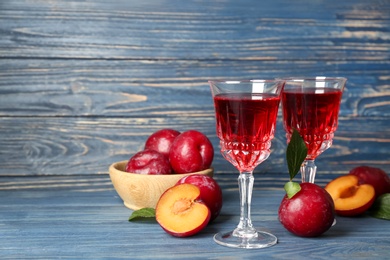 Delicious plum liquor and ripe fruits on blue wooden table. Homemade strong alcoholic beverage