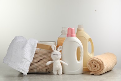 Photo of Bottles of laundry detergents, fresh towels, knitted rabbit toy on grey table against white background