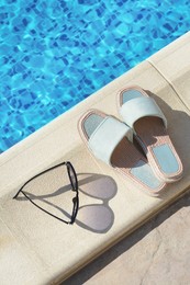 Photo of Stylish sunglasses and slippers at poolside on sunny day. Beach accessories