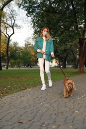Woman in protective mask with English Cocker Spaniel in park. Walking dog during COVID-19 pandemic
