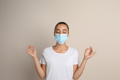 Woman in protective mask meditating on beige background. Dealing with stress caused by COVID‑19 pandemic