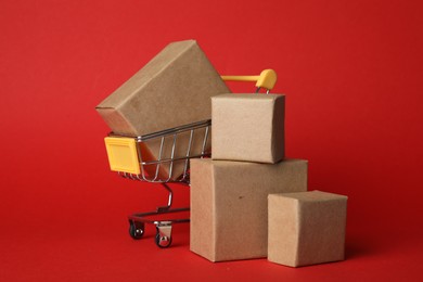 Photo of Shopping cart and boxes on red background. Logistics and wholesale concept