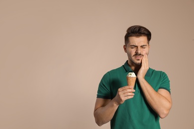 Emotional young man with sensitive teeth and ice cream on color background. Space for text