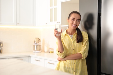Young woman holding glass of pure water in kitchen. Space for text