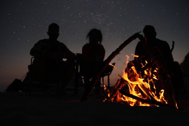 Group of friends gathering around bonfire in evening, focus on flame. Camping season
